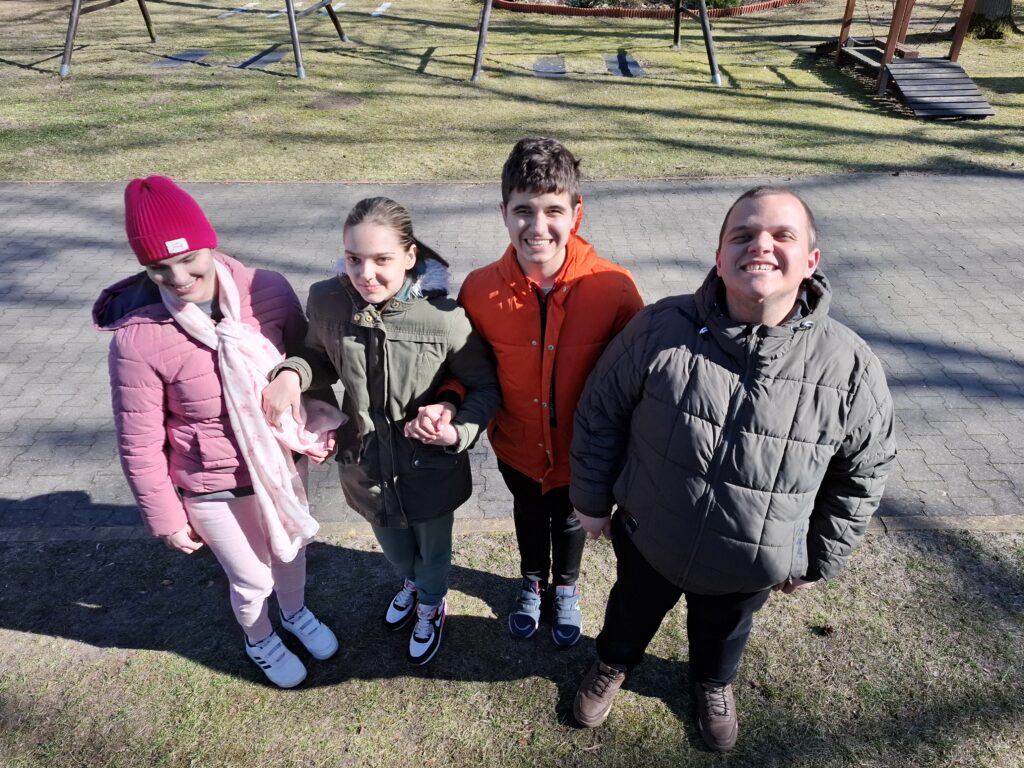 Dwie uczennice wraz z dwoma kolegami z uśmiechem na twarzy patrzą w górę na placu zabaw.