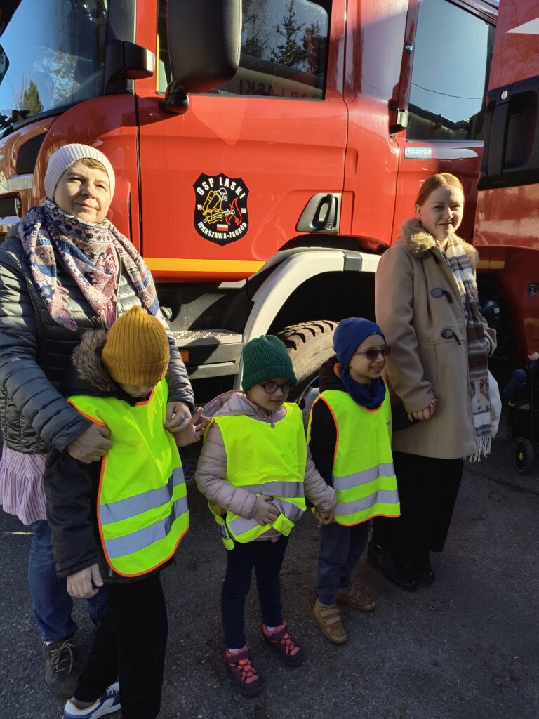 Przedszkolaki z dwoma paniami na tle wozu strażackiego.
