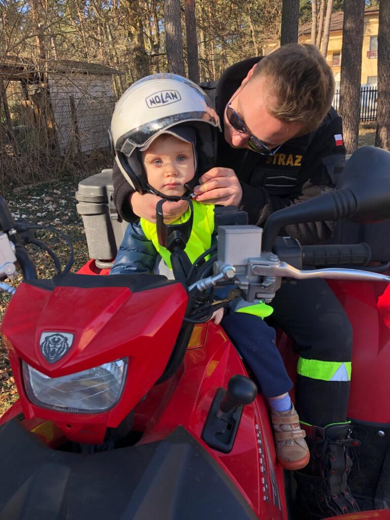 Strażak zapina kask  przedszkolakowi  na quadzie.