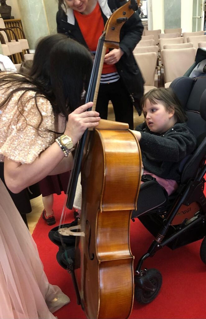 Dziewczynka ogląda wiolonczelę trzymaną przez artystkę z filharmonii.