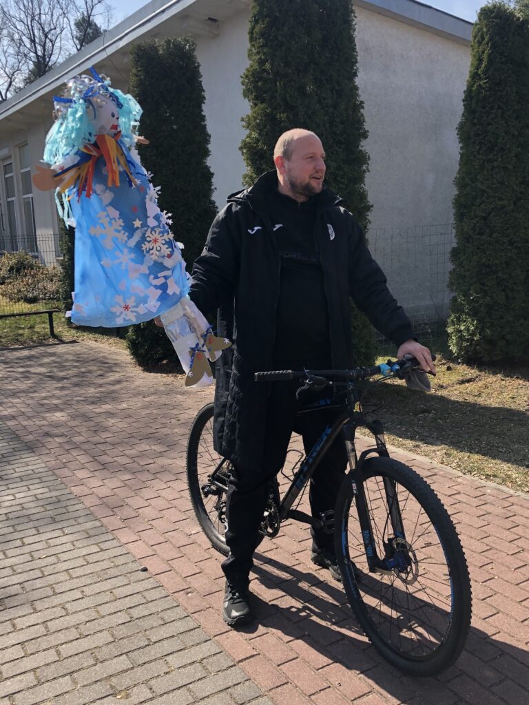 Uśmiechnięty rowerzysta trzyma kukiełkę Pani Zimy.