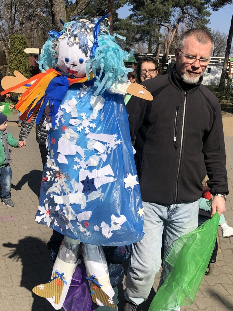 Terapeuta pomaga chłopcu nieść kukiełkę Pani Zimy.