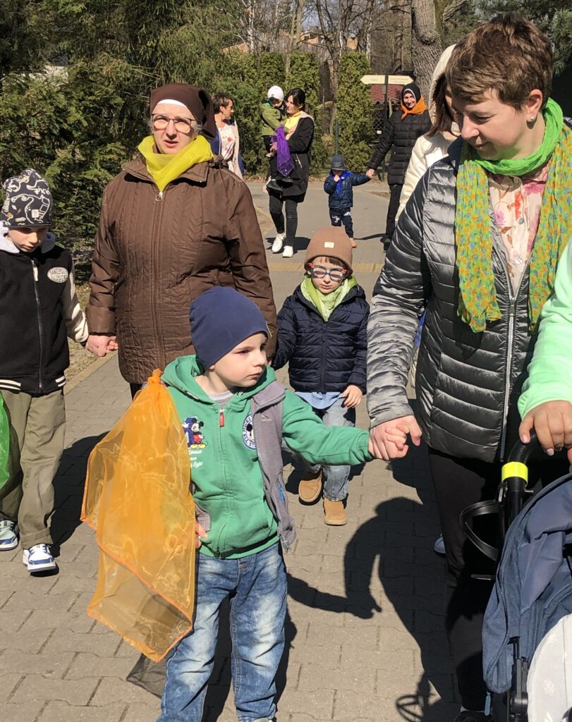 Dzieci i nauczycielki z kolorowymi chustami idą chodnikiem.
