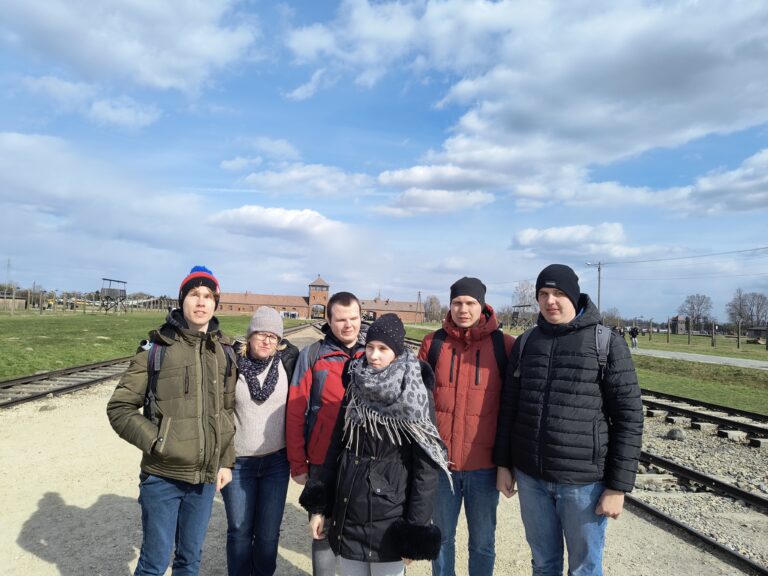 Grupa na tle bramy prowadzącej do obozu Auschwitz-Birkenau.