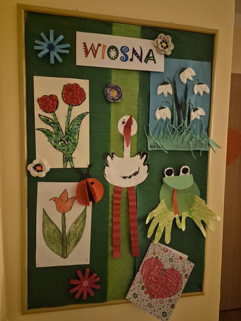 W grupie 8 gazetka na której wiszą wiosenne kwiaty przebiśniegi, tulipany, bocian, żaba.
