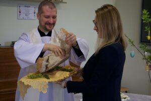 Ks. Sebastian przy pomocy dyrektor Kamili łamią chleb na kawałki.