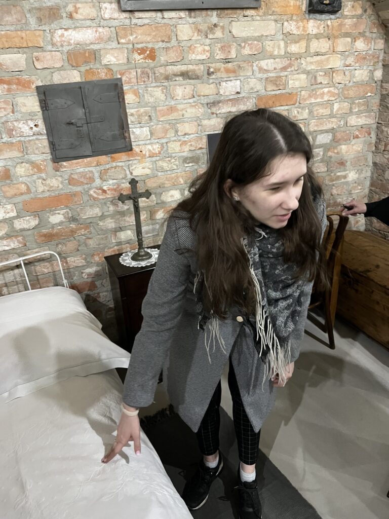 Amelia oglądająca rekonstrukcję celi św. siostry Faustyny, uczennica dotyka łóżka z siennikiem
