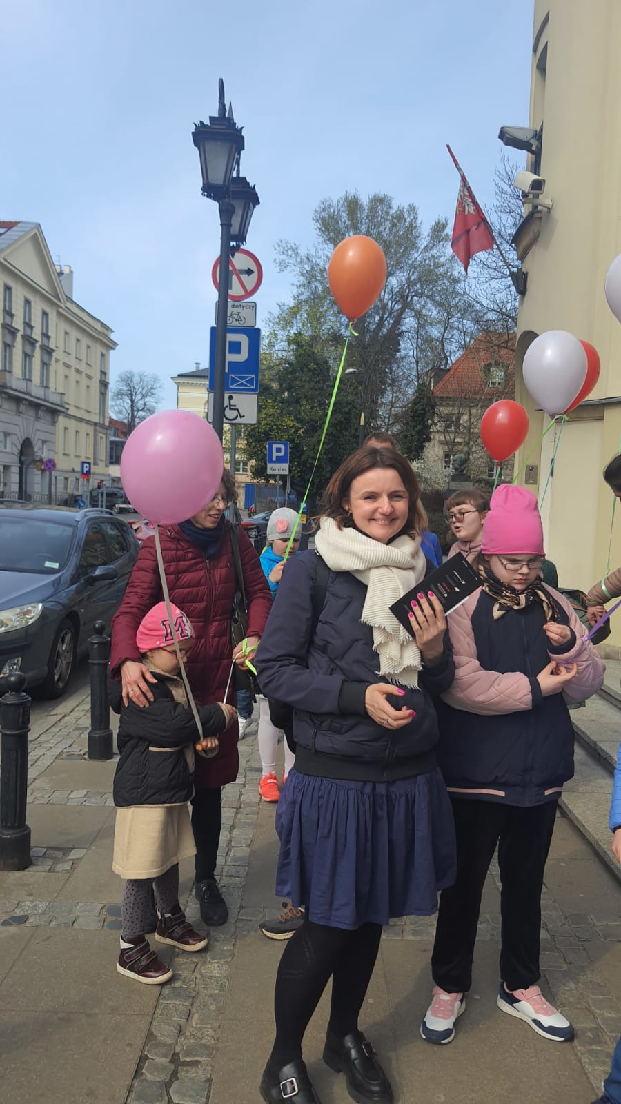 Osoby z balonami na chodniku przed teatrem