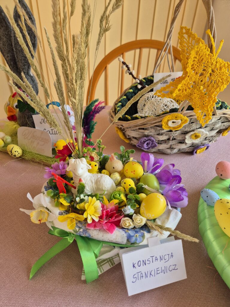 Kolorowe stroiki na stole a na pierwszym planie stroik Konstancji Stankiewicz z grupy 8. To strok w formie koszyczka w którym znajdują się: baranek, pisanki, kurczaczki , kwiatki.