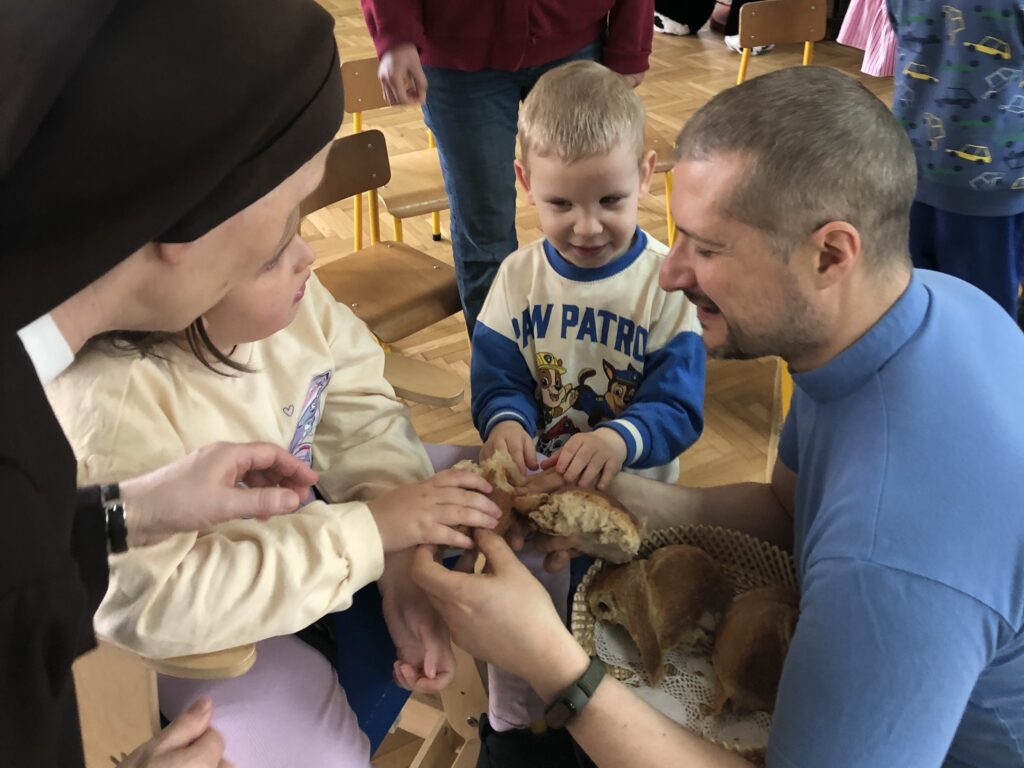 Ksiądz dzieli się chlebem z dziećmi i Siostrą. 