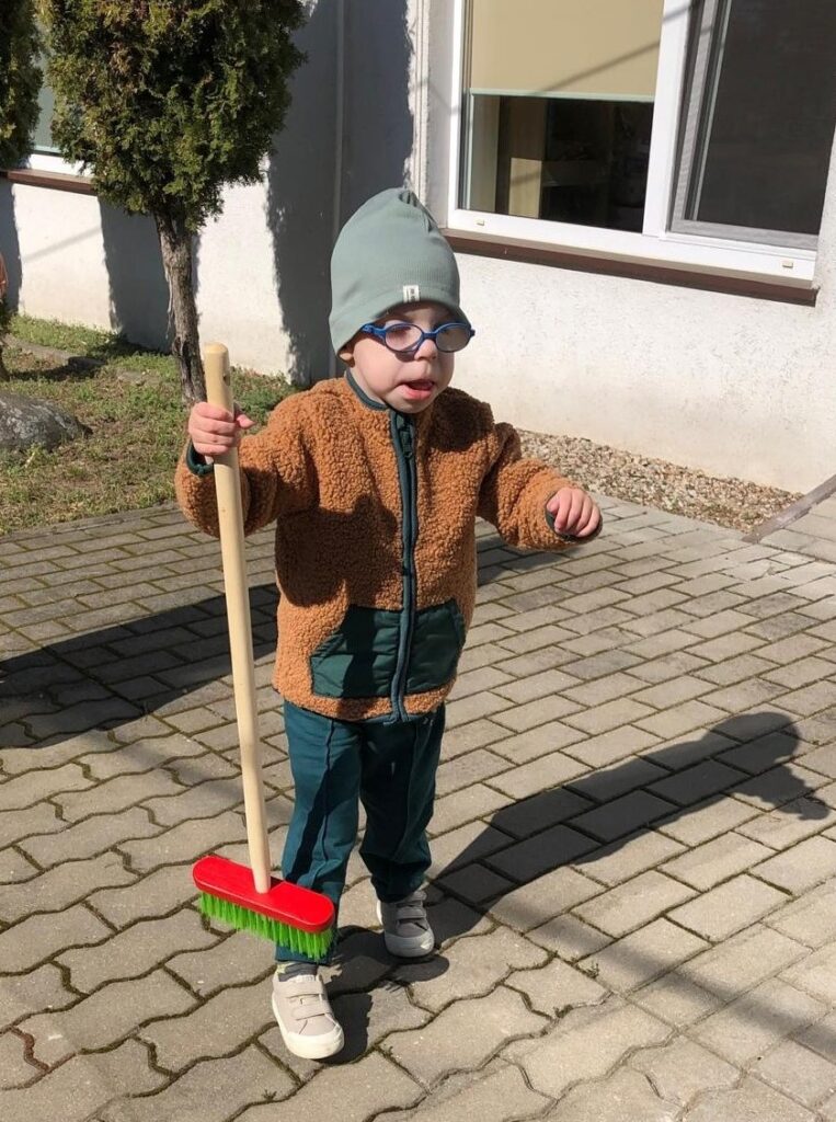 Chłopiec ze szczotką w dłoni stoi na chodniku.