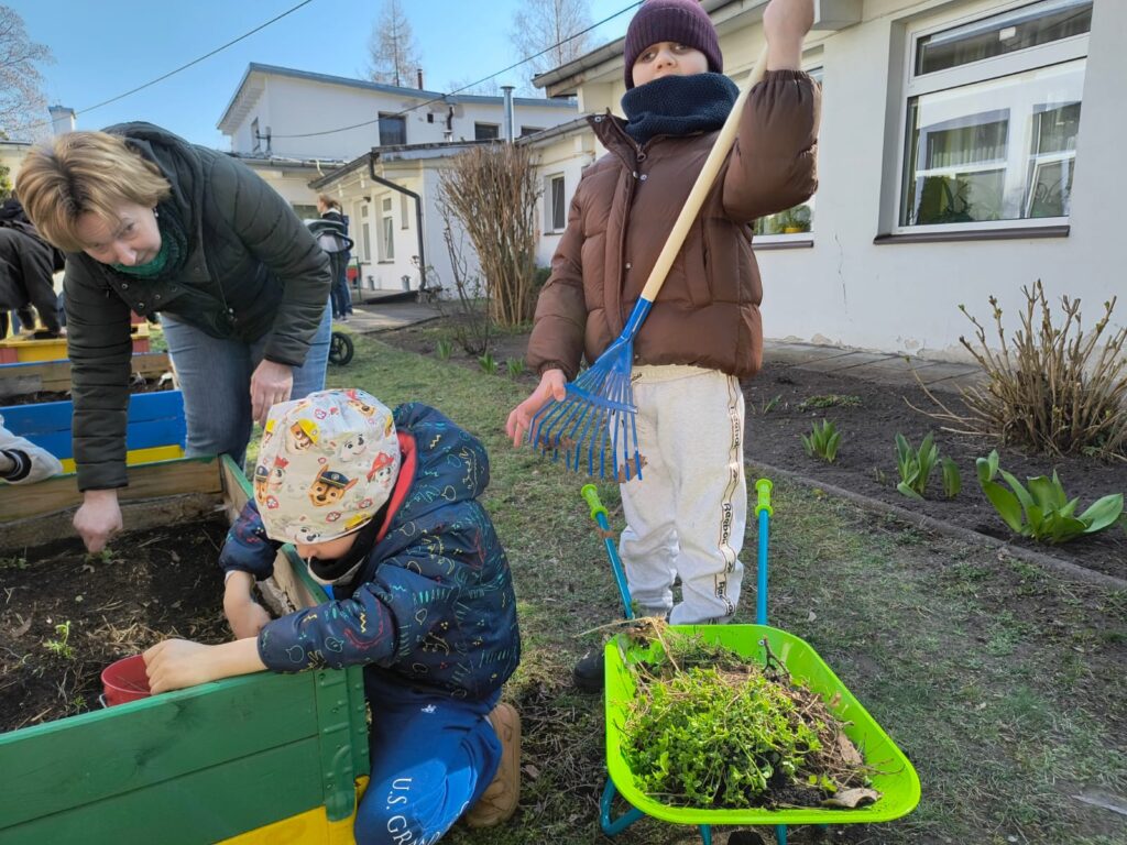 Dzieci z nauczycielką pomagają robić porządki w ogródku