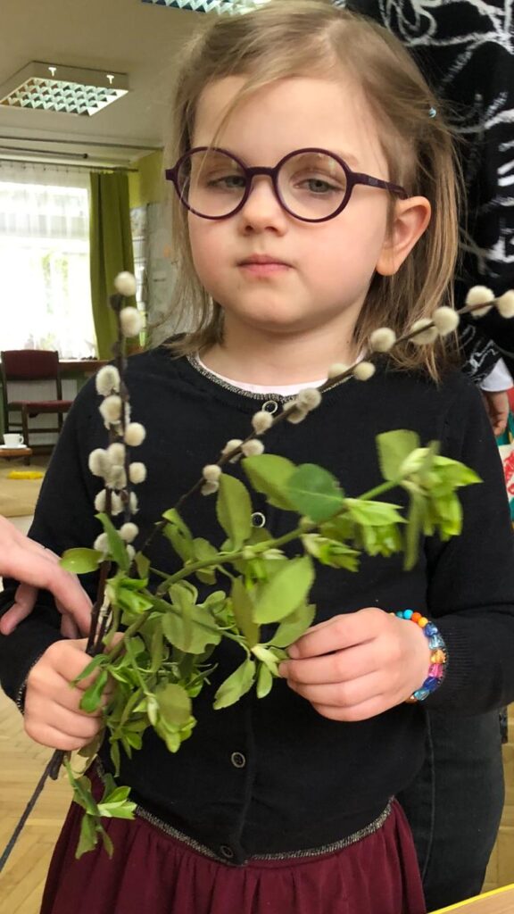 Dziewczynka trzyma w dłoni zielone gałązki i bazie.