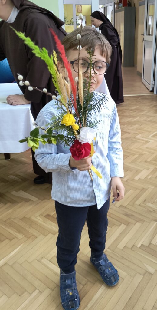 Chłopiec trzyma w dłoni zrobioną palemkę wielkanocną.