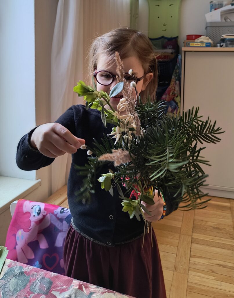 Dziewczynka trzyma w dłoni zrobioną palemkę wielkanocną.