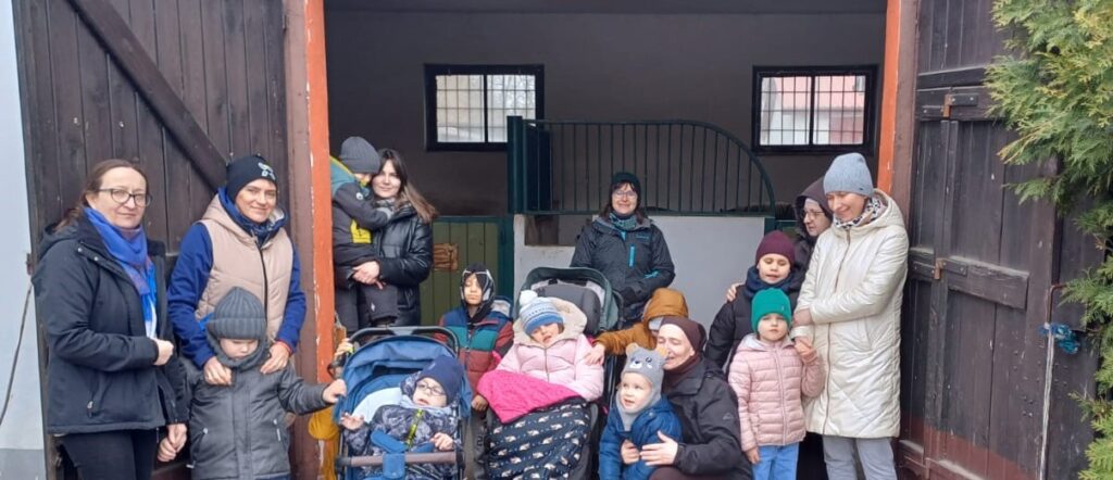 Dzieci i nauczyciele stoją w otwartych drzwiach do stajni. 