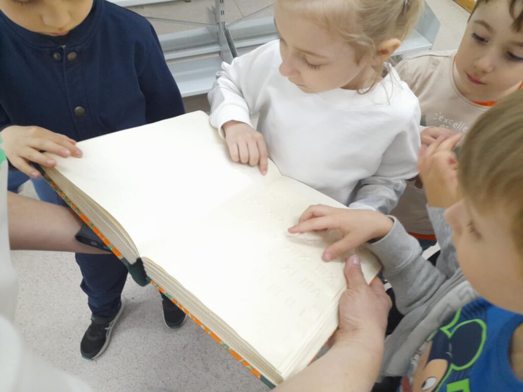 dzieci dotykające znaków brajlowskich w książce