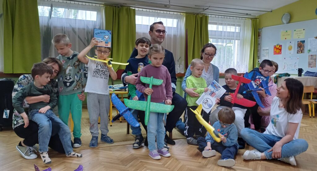 Dzieci trzymające w rękach samoloty, z panem pilotem i nauczycielkami
