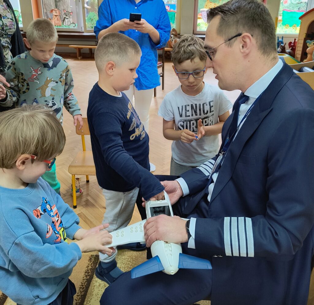 Dzieci z panem pilotem, dotykają zabawkowego samolotu