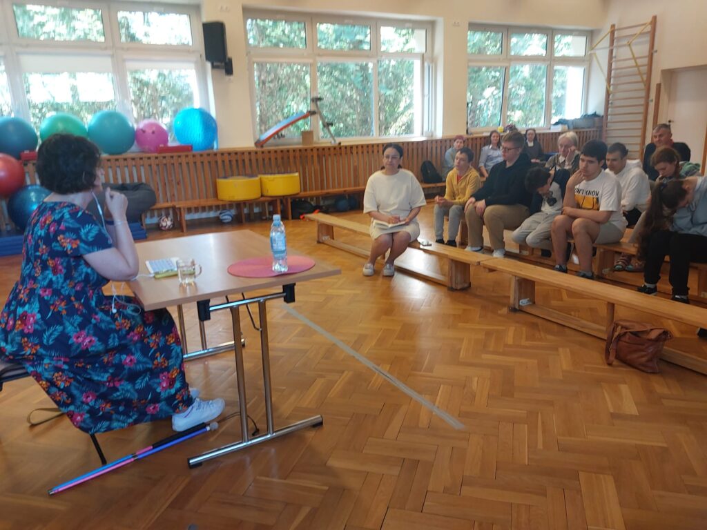 Kobieta siedząca przy stole, naprzeciwko słuchającej jej młodzieży
