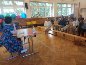 Kobieta siedząca przy stole, naprzeciwko słuchającej jej młodzieży