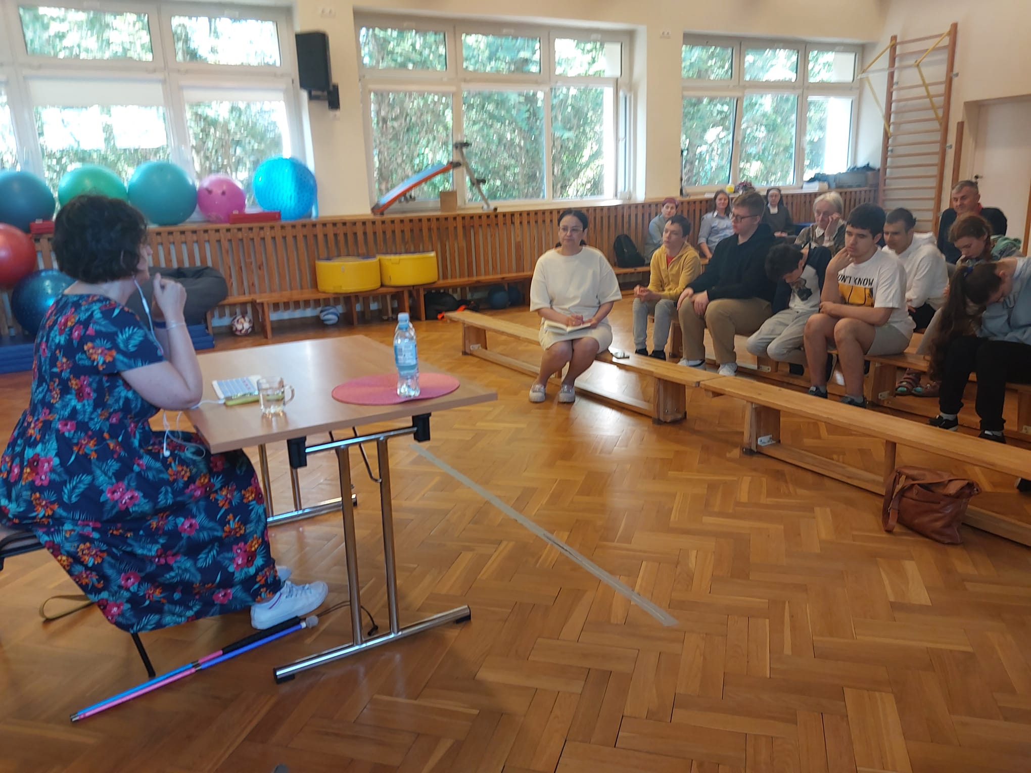Kobieta siedząca przy stole, naprzeciwko słuchającej jej młodzieży