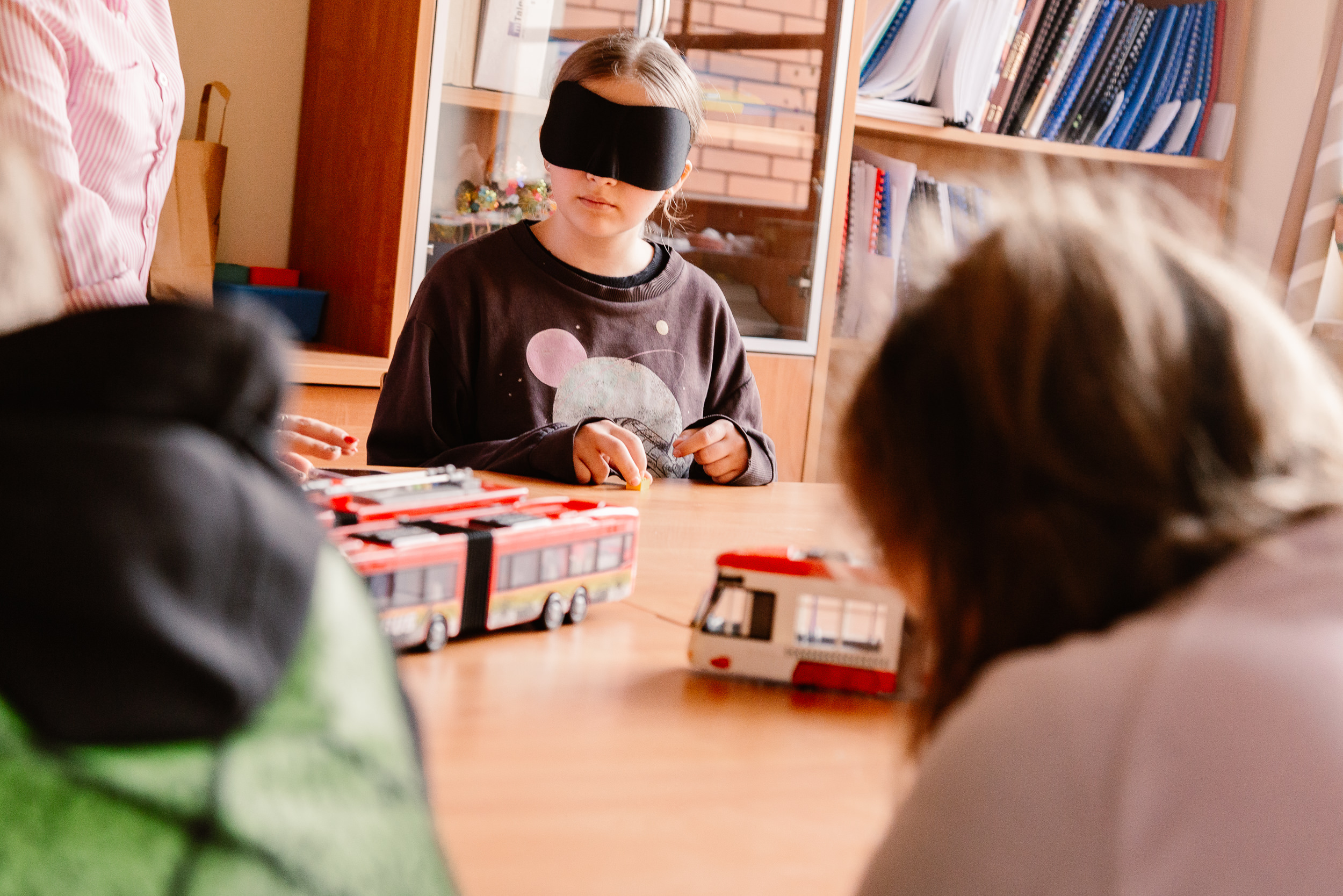 Dziewczynka z opaską na oczach siedzi przy ławce