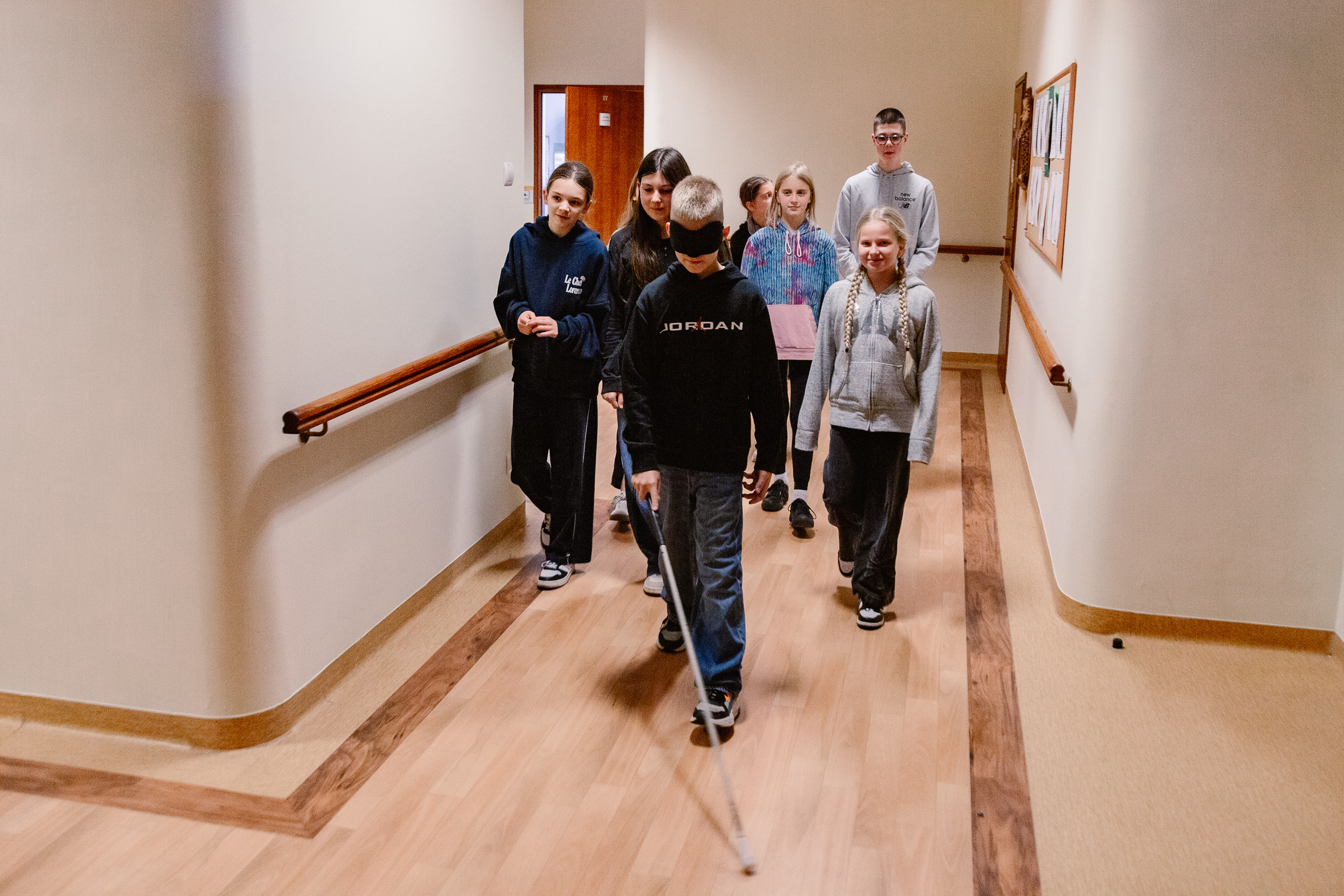 Chłopiec z opaską na oczach i białą laską idzie korytarzem