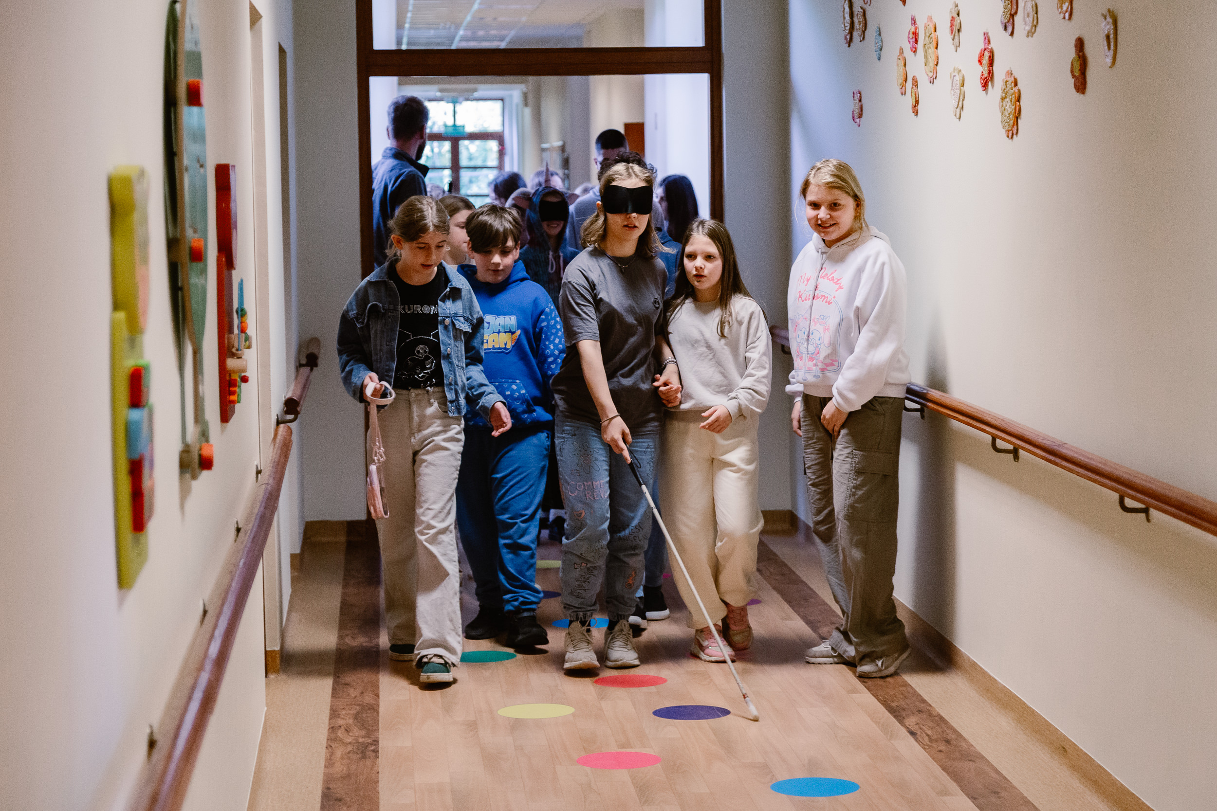 Dzieci w opaskach z laską w ręku przemierzają korytarz