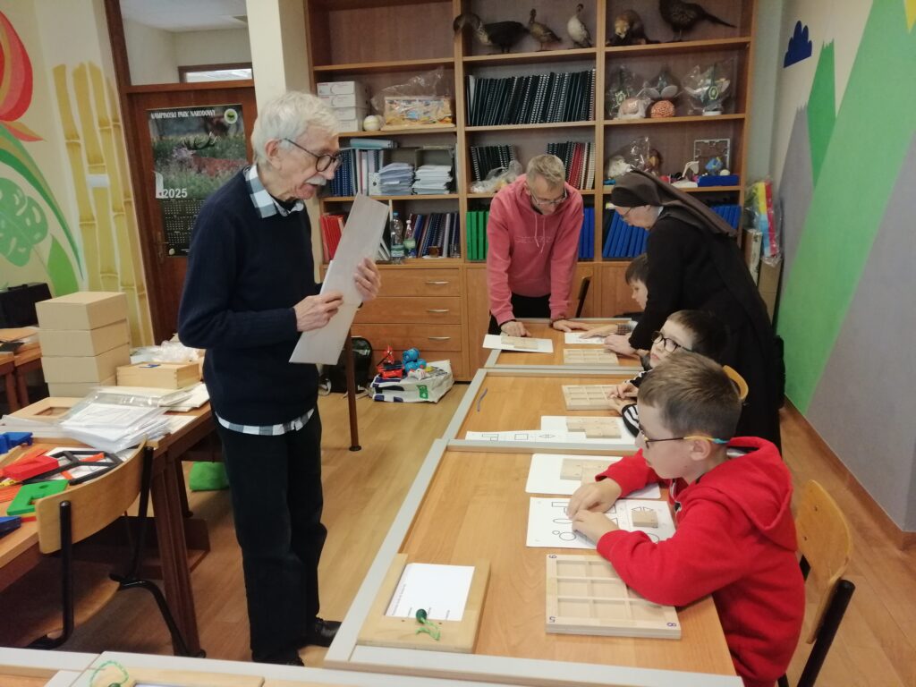 Panowie z Fundacji wraz z Siostrą tłumaczą uczniom 3 klasy jak mają rozpoznać bryły geometryczne.