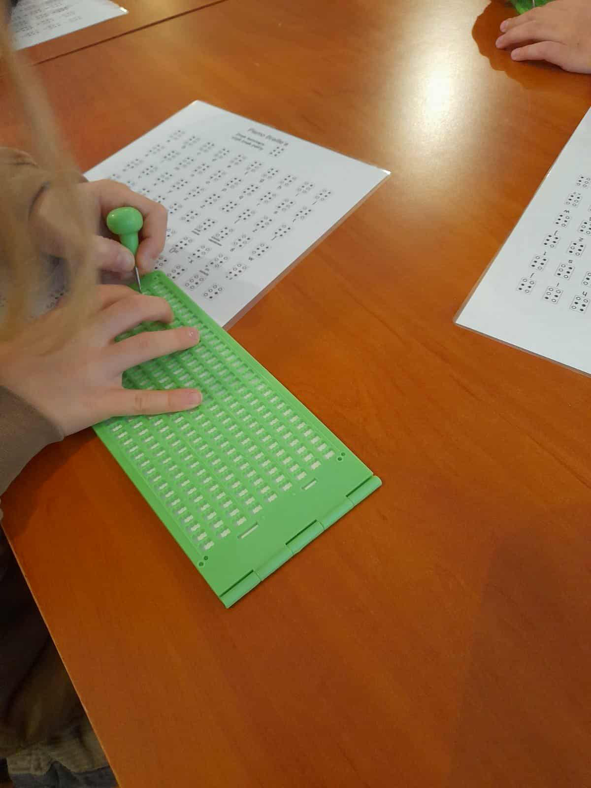 Uczeń pisze na tabliczce brajlowskiej