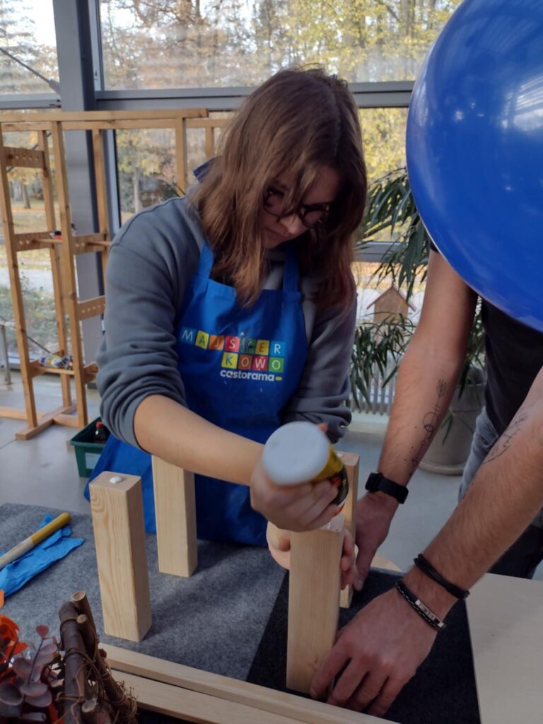 Na zdjęciu uczennica klei drewnianą konstrukcje. 