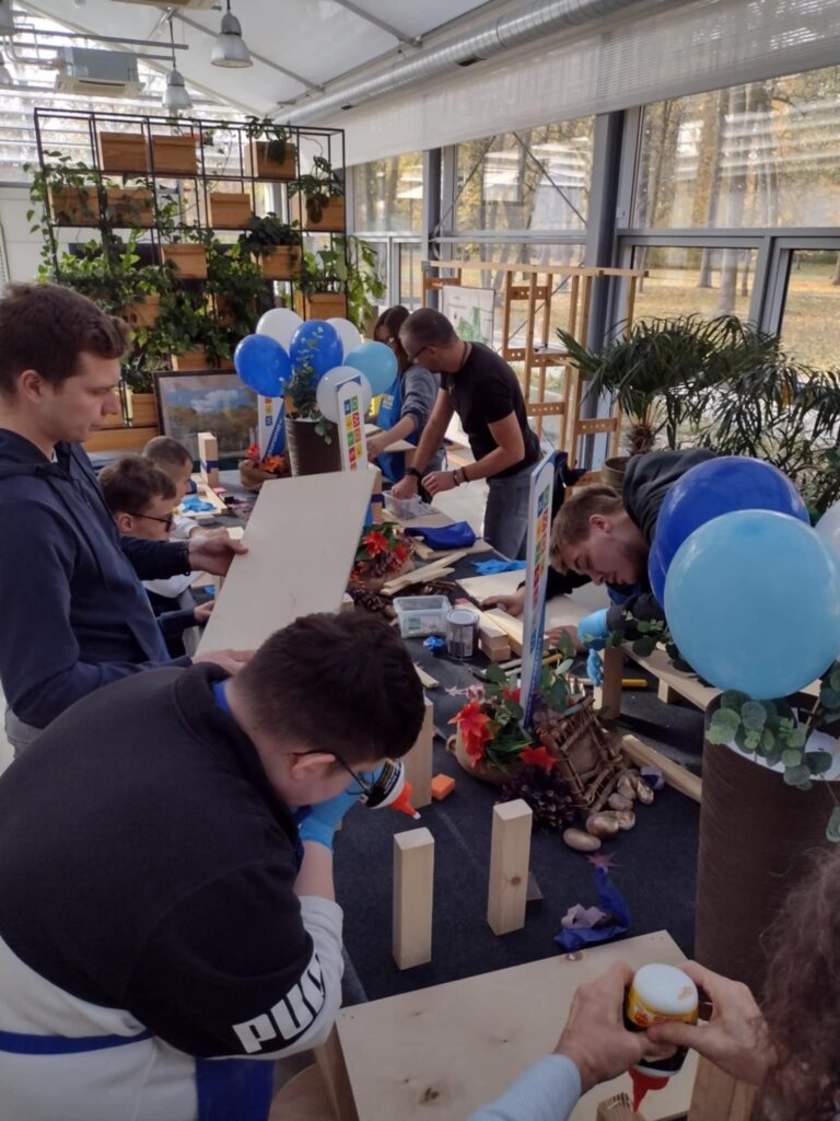 Na zdjęciu uczniowie kleją przy stole drewnianą konstrukcje. 