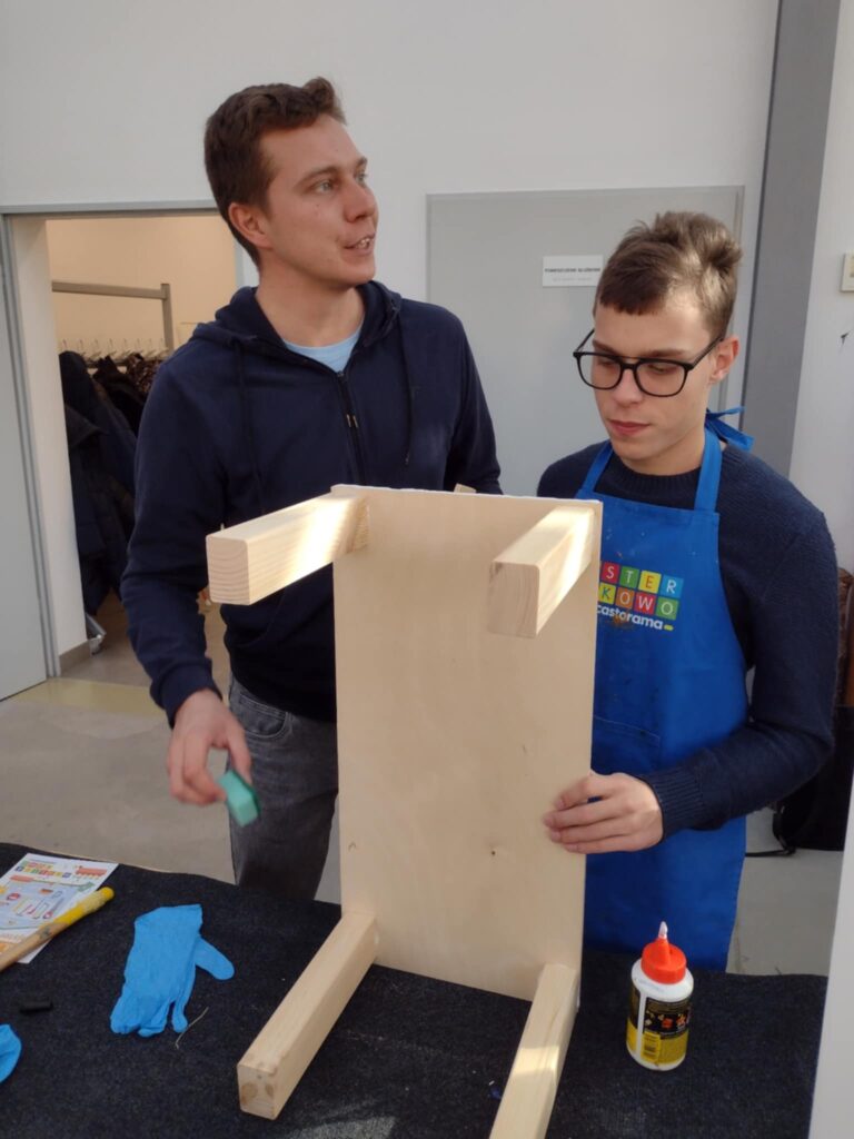 Na zdjęciu uczeń z pomocą nauczyciela sprawdza kształt drewnianej konstrukcji.