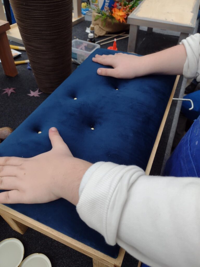 Na zdjęciu uczennica dotyka siedzenia niezrobionego dla drewnianej konstrukcji. 