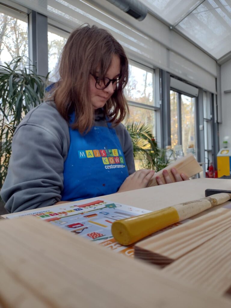 Na zdjęciu uczennica dotyka  drewniane klocki. Siedzi przy stole.
