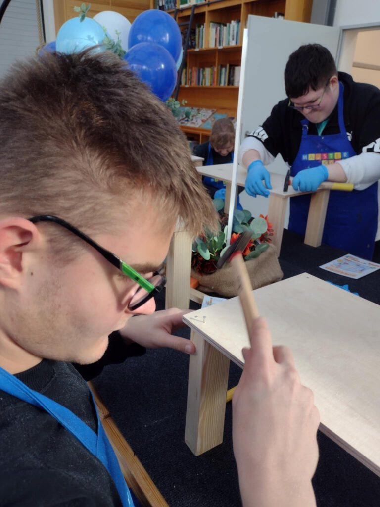 Na zdjęciu uczniowie przybijają gwoździe do krzesełka drewnianego.