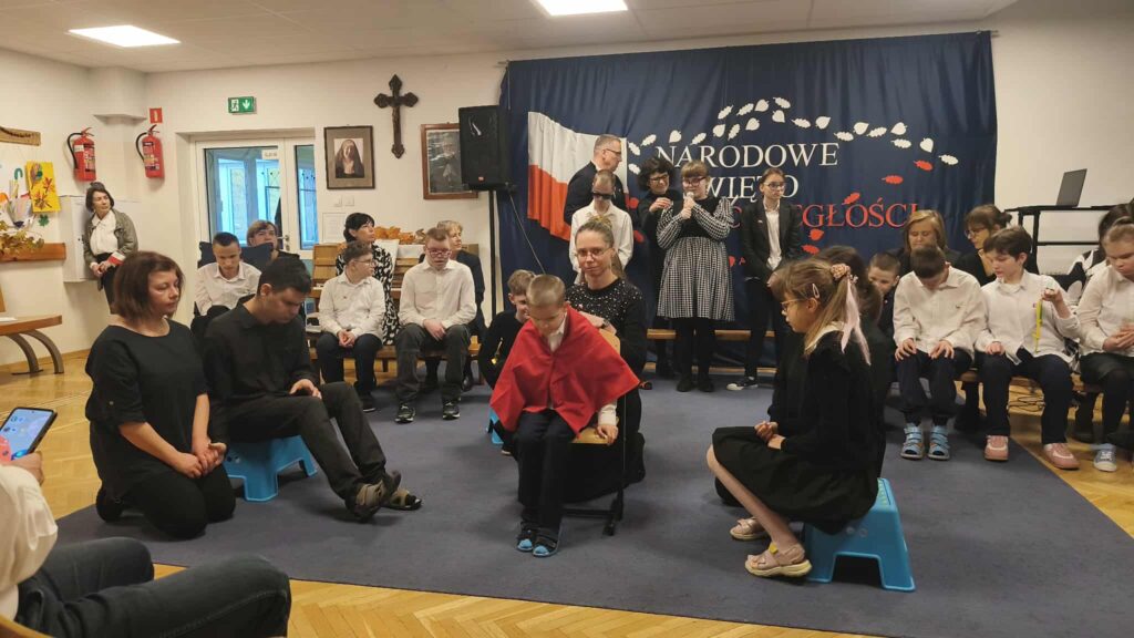 Uczniowie siedzą na środku sali i uczniowie wypowiadają swoje kwestie