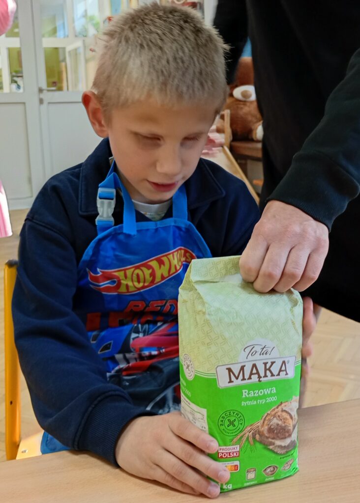 Chłopiec siedzi przy stole , dotyka mąki w papierowym opakowaniu.