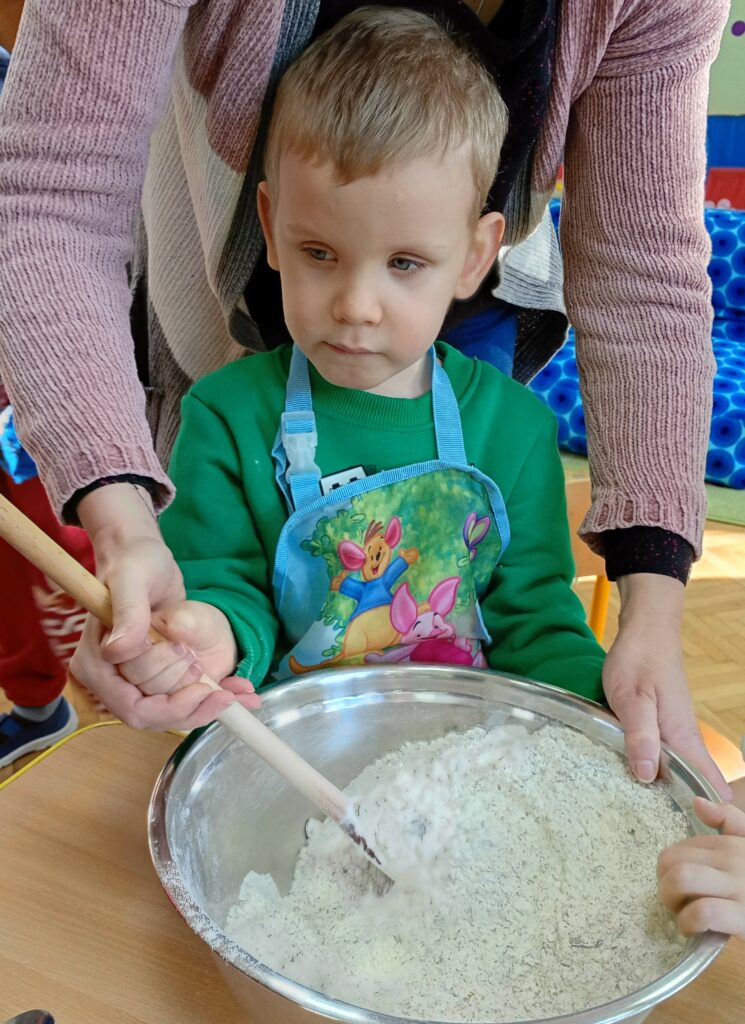 Chłopiec stoi przy stole, miesza w misce składniki na chleb.