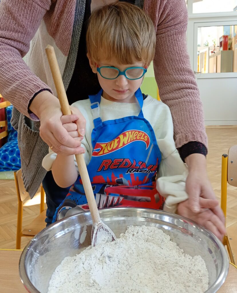 Chłopiec stoi przy stole, miesza w misce składniki na chleb.