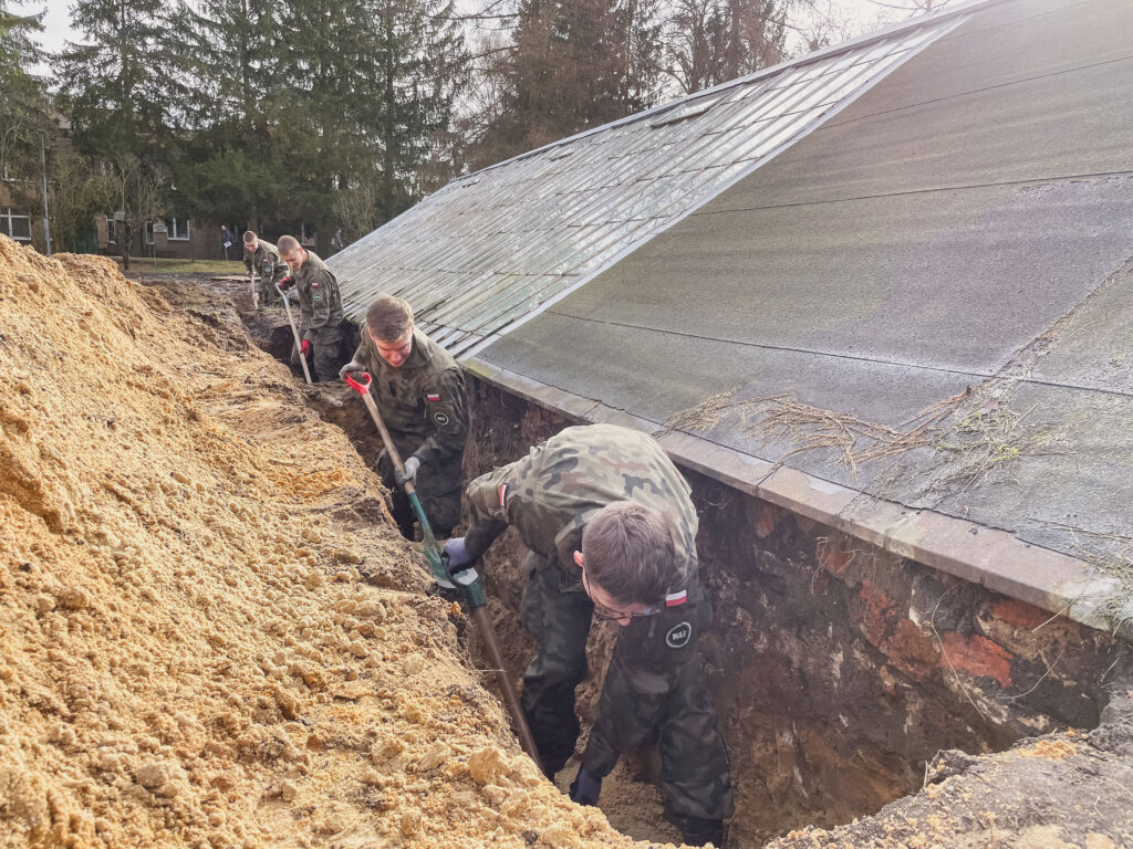 wolontariusze w mundurach wykopują rów łopatami