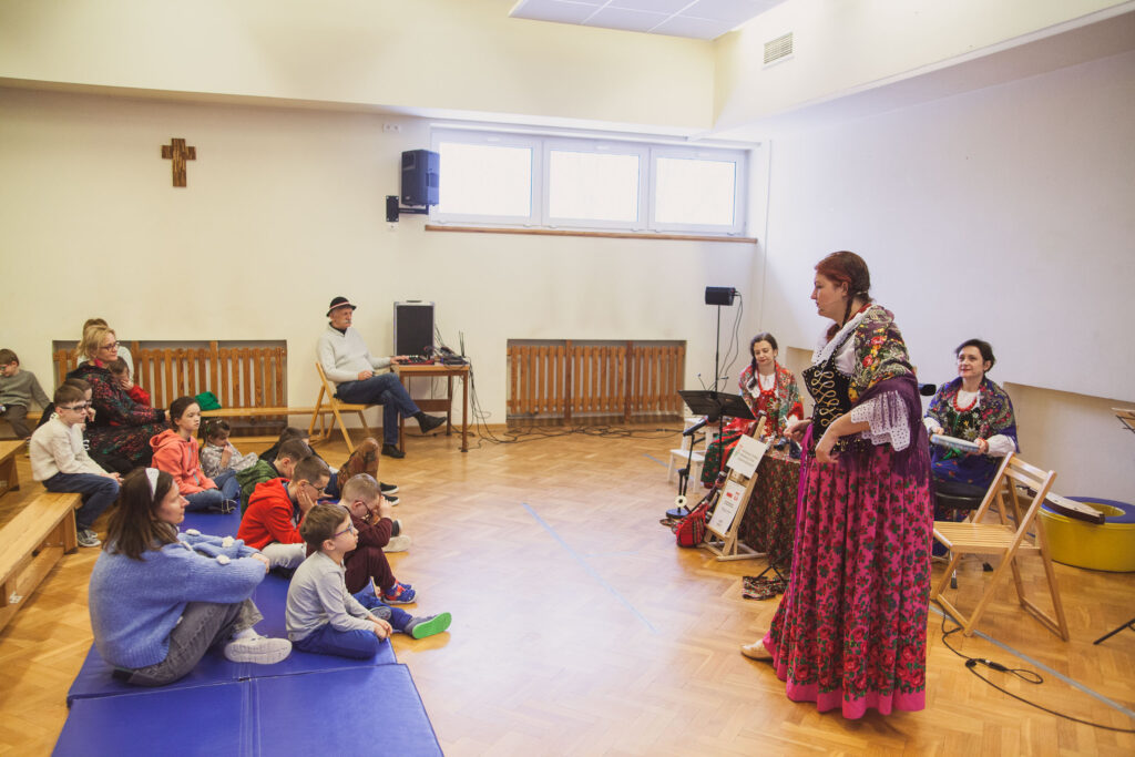 występ w sali gimnastycznej, wykonawcy na scenie i uczniowie na widowni