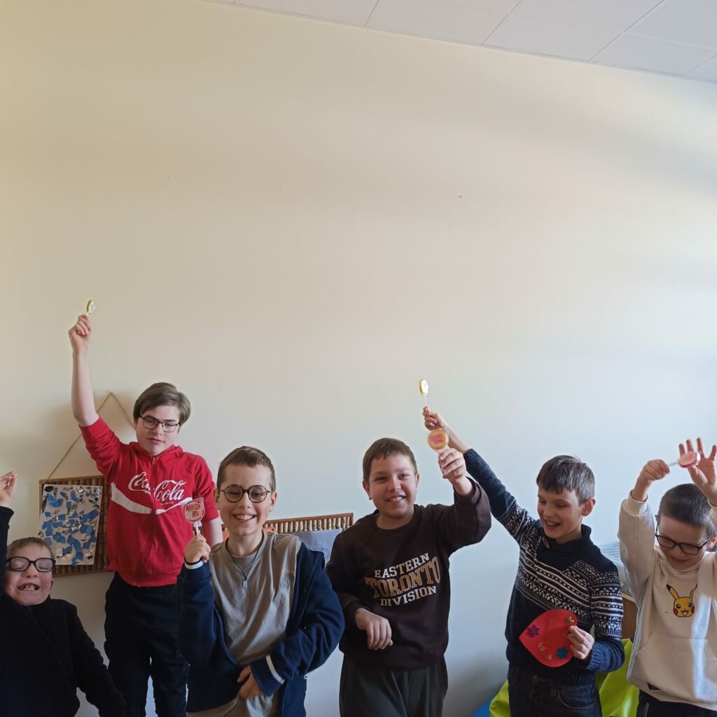 Czworo uśmiechniętych uczniów w okularach stoi w rzędzie, dumnie prezentując własnoręcznie wykonane, kolorowe serca z papieru oraz otrzymane walentynkowe upominki.