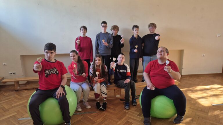 Grupa starszych uczniów pozuje w sali gimnastycznej, siedząc na zielonych piłkach rehabilitacyjnych i ławkach, trzymając w dłoniach walentynkowe lizaki otrzymane od Pani Dyrektor.