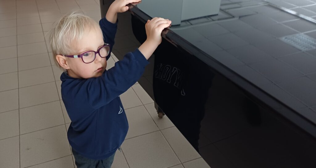 Mały chłopiec stoi przy fortepianie.