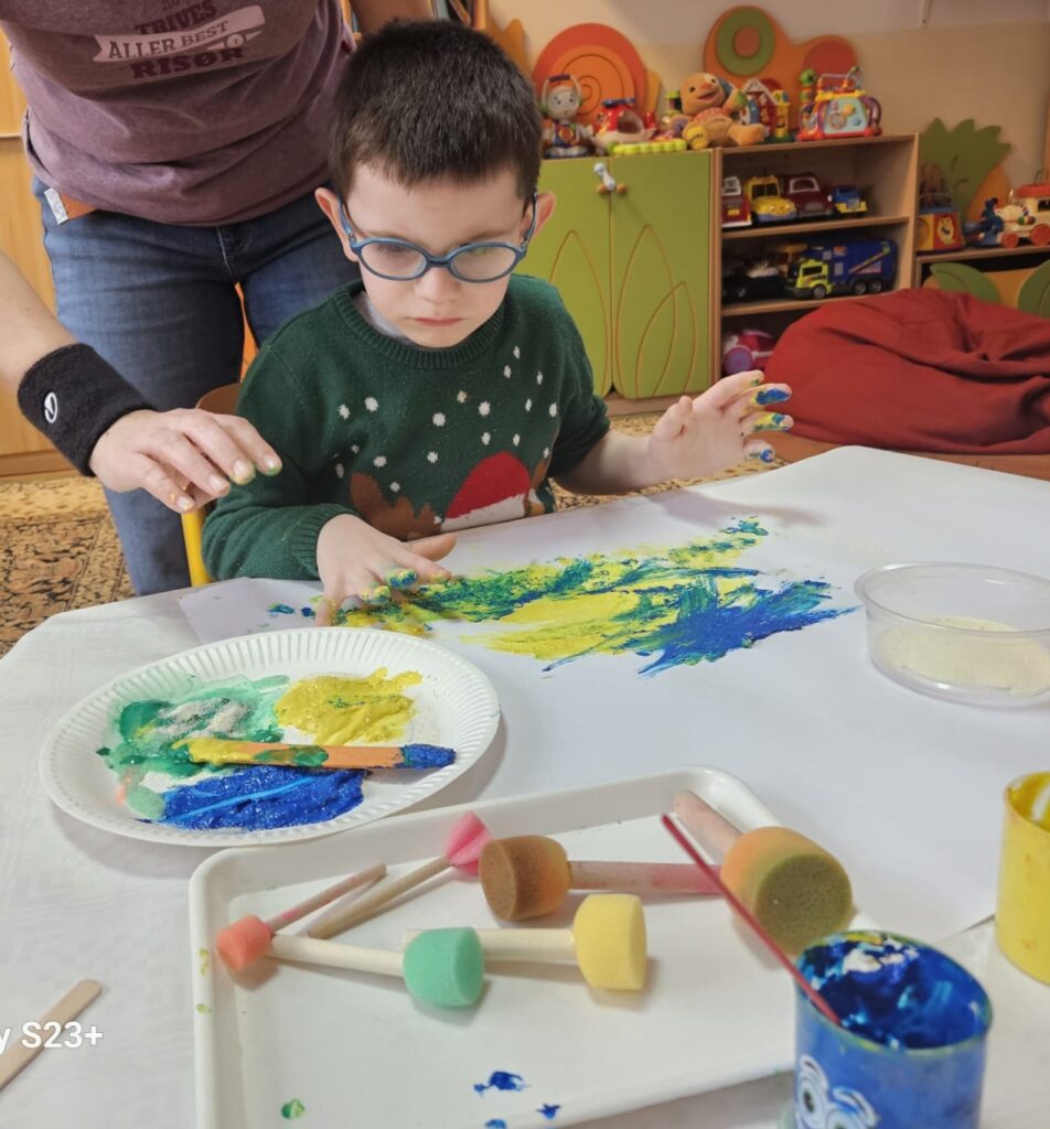 Chłopiec przy stole maluje rękami.