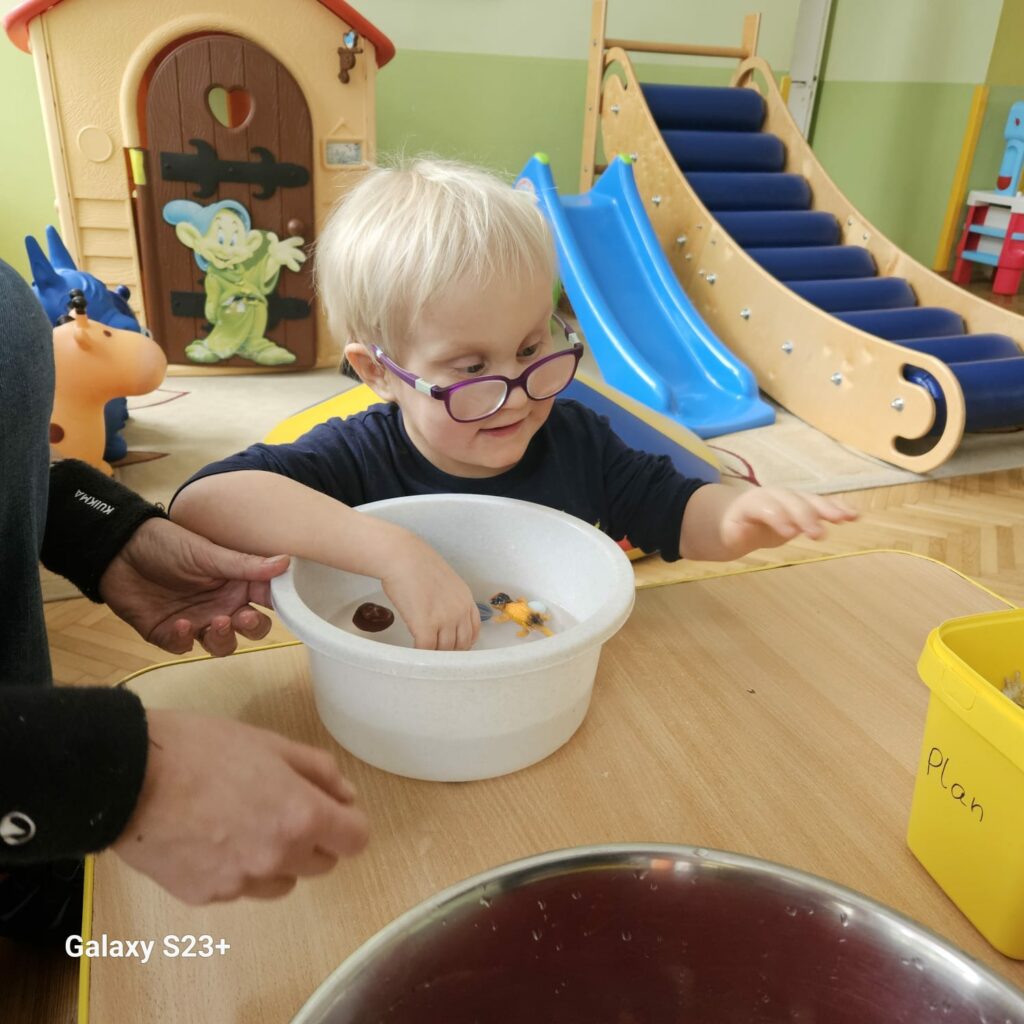 Chłopiec trzyma rękę w miednicy z wodą w której pływają zabawki.