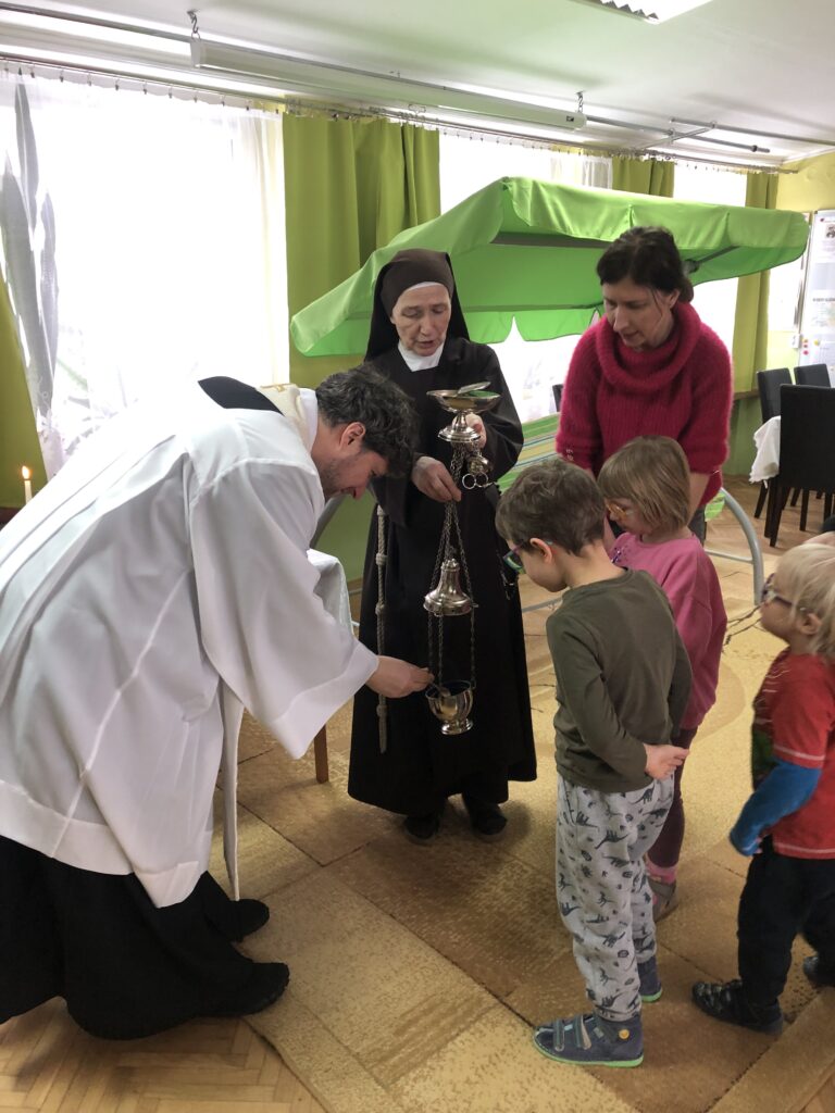 Ksiądz napełnia trybularz trzymany przez siostrę.. Obok stoją dzieci i nauczycielka.