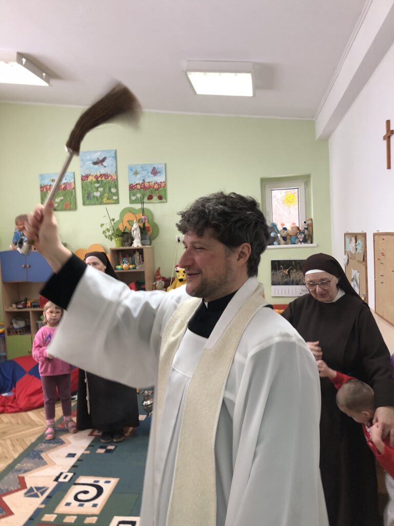 Ksiądz z kropidłem w dłoni, święci salę.